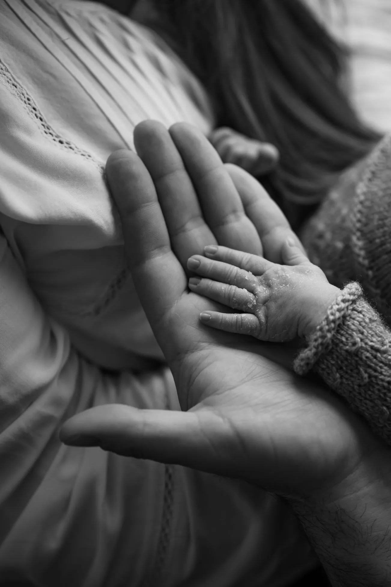 An infant’s hand resting in an adult’s open palm, in black and white